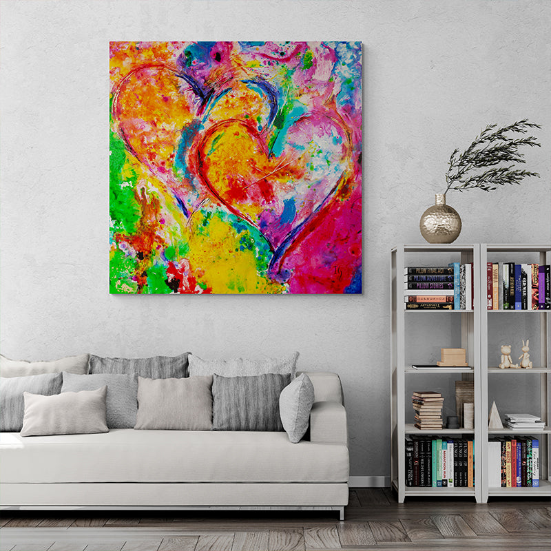 Passionate Symphony – Abstract painting of two intertwined hearts in vivid red, yellow, blue, and green, displayed in a modern living room with a white sofa and bookshelf. A bold and colorful expression of love and passion.